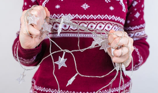 Woman in red holiday sweater holding tangled holiday lights