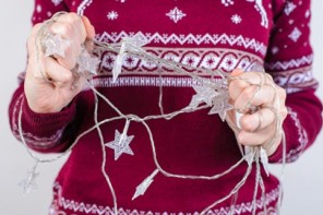 Woman in red holiday sweater holding tangled holiday lights