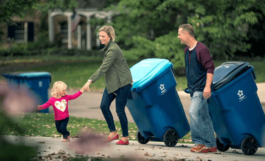 Toddler pulling her mom hand, while both parents pull waste and recycling containers